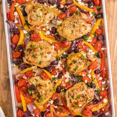 cooked greek chicken with feta cheese and roasted vegetables on a sheet pan