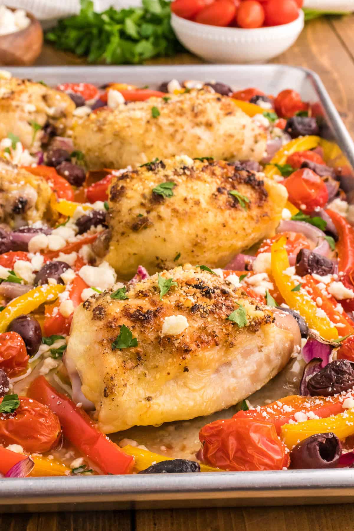 greek chicken thighs on a sheet pan surrounded by red and yellow peppers