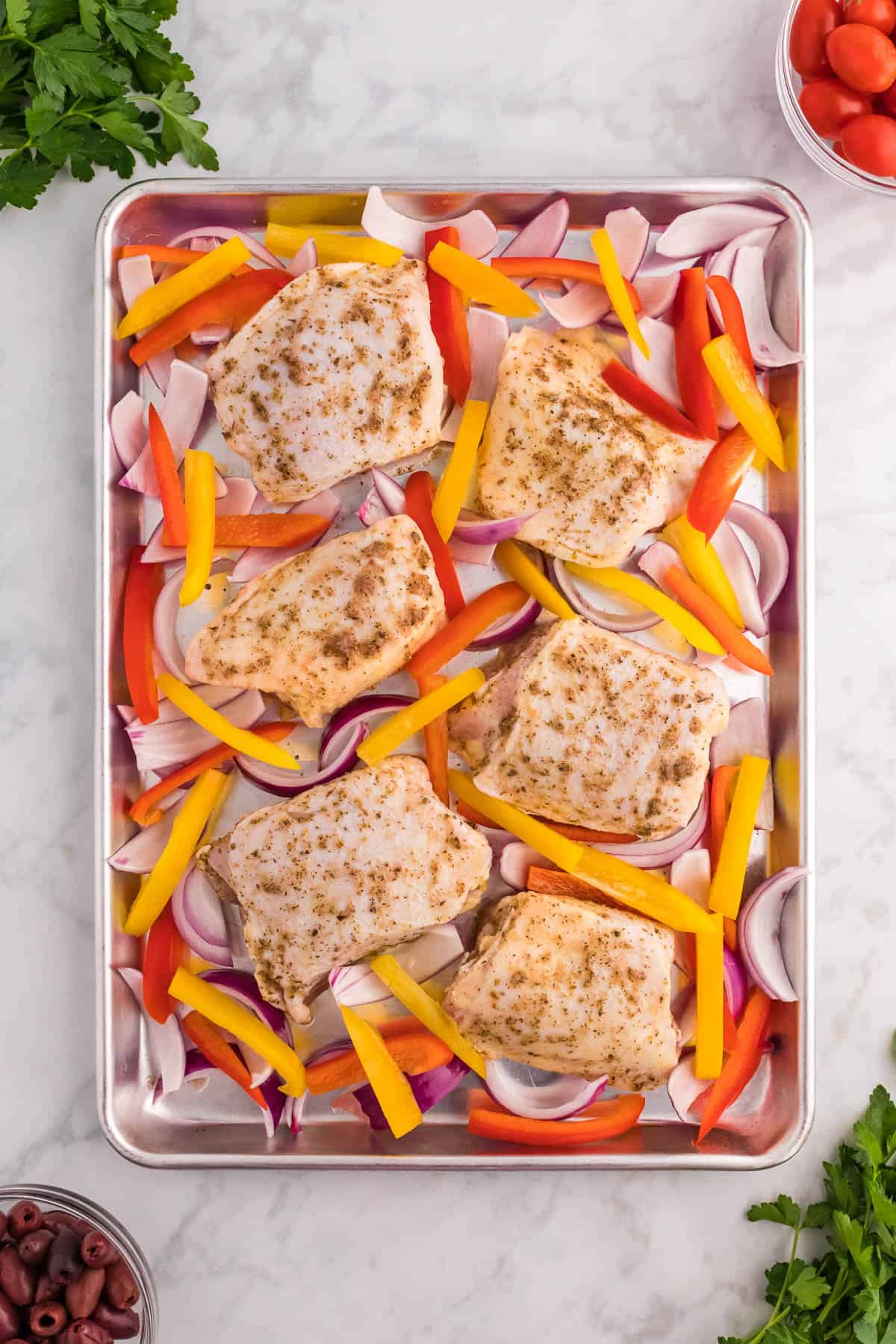 Place the sliced red onion, red bell pepper, and yellow bell pepper around the chicken on the sheet pan.