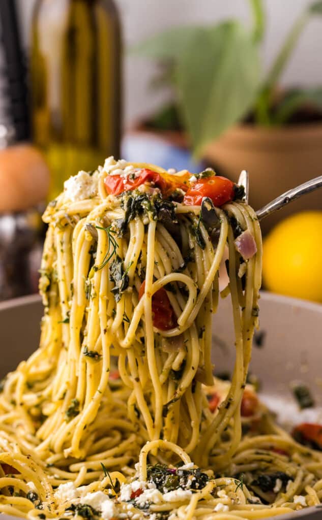 spaghetti being lifted with herbs and tomatoes