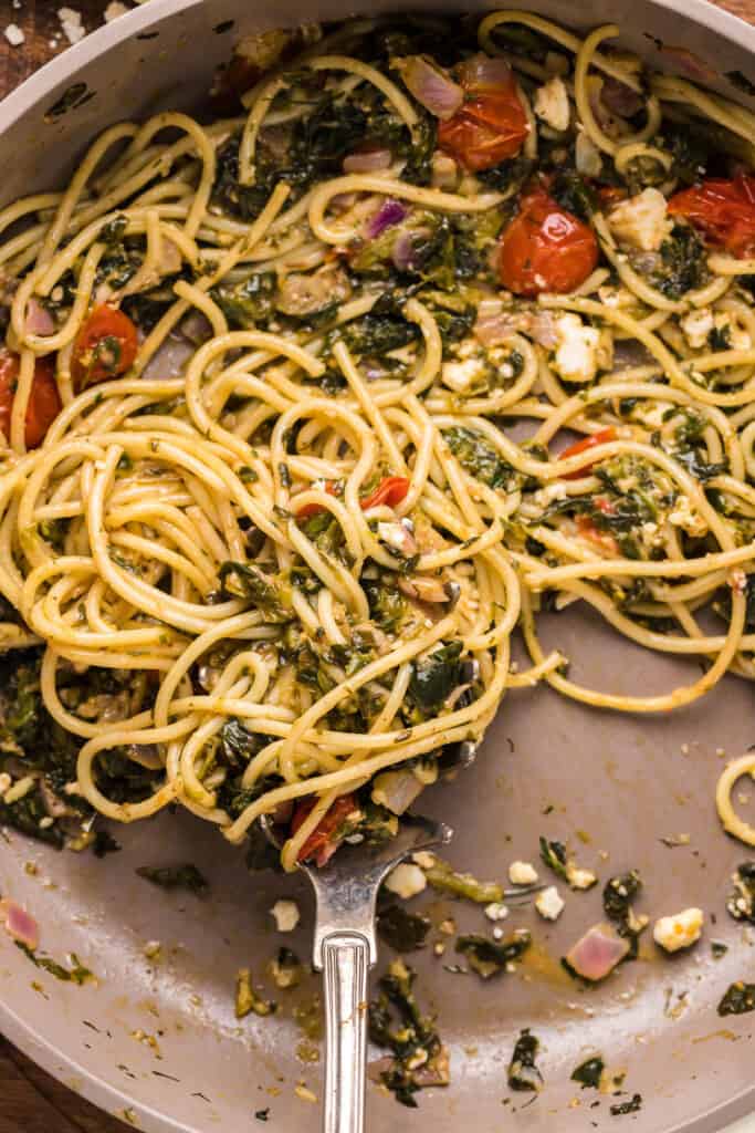 a fork twirling cooking spaghetti and herbs