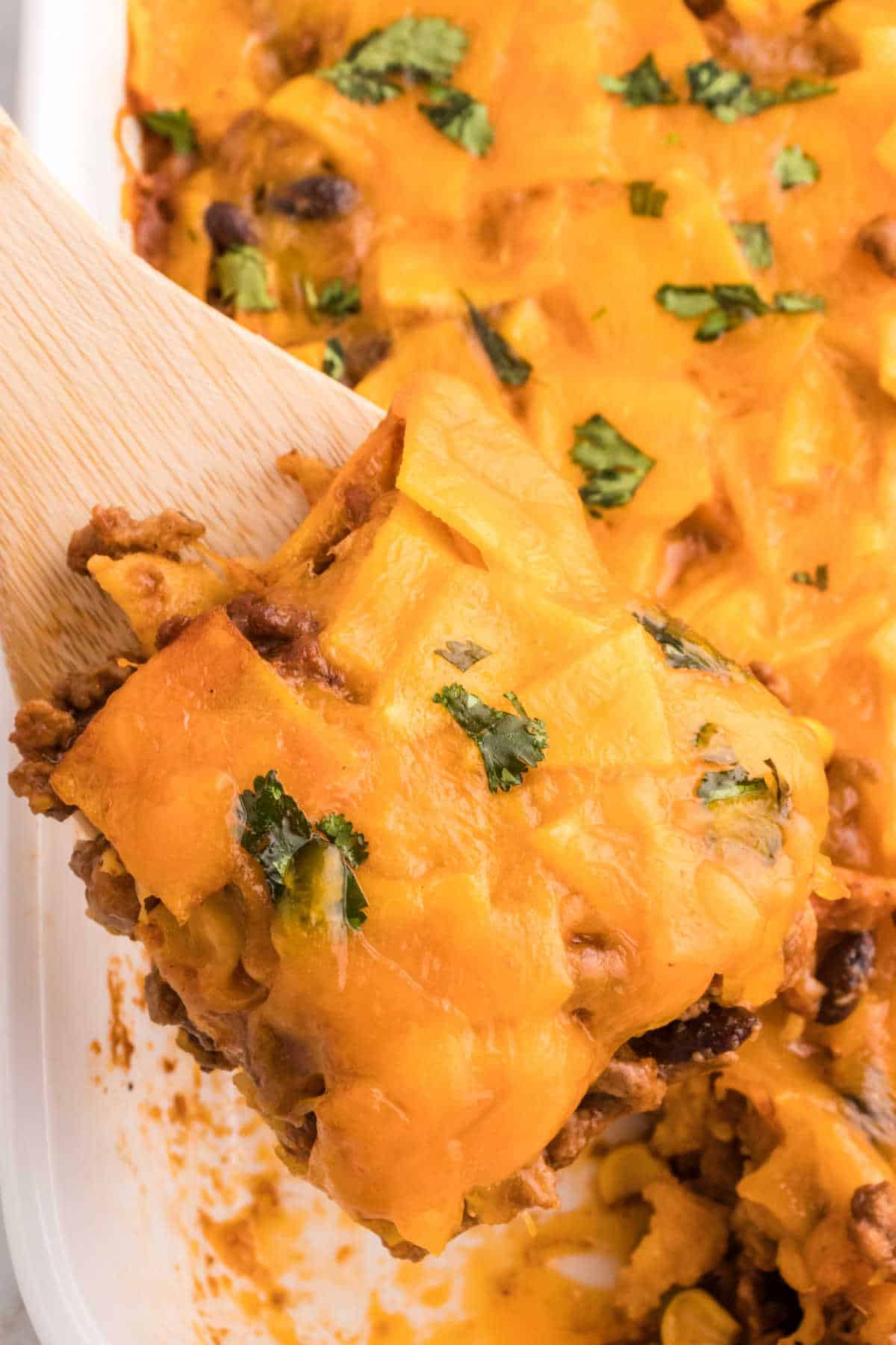 A wooden serving spoon serving a piece of beef enchilada casserole.