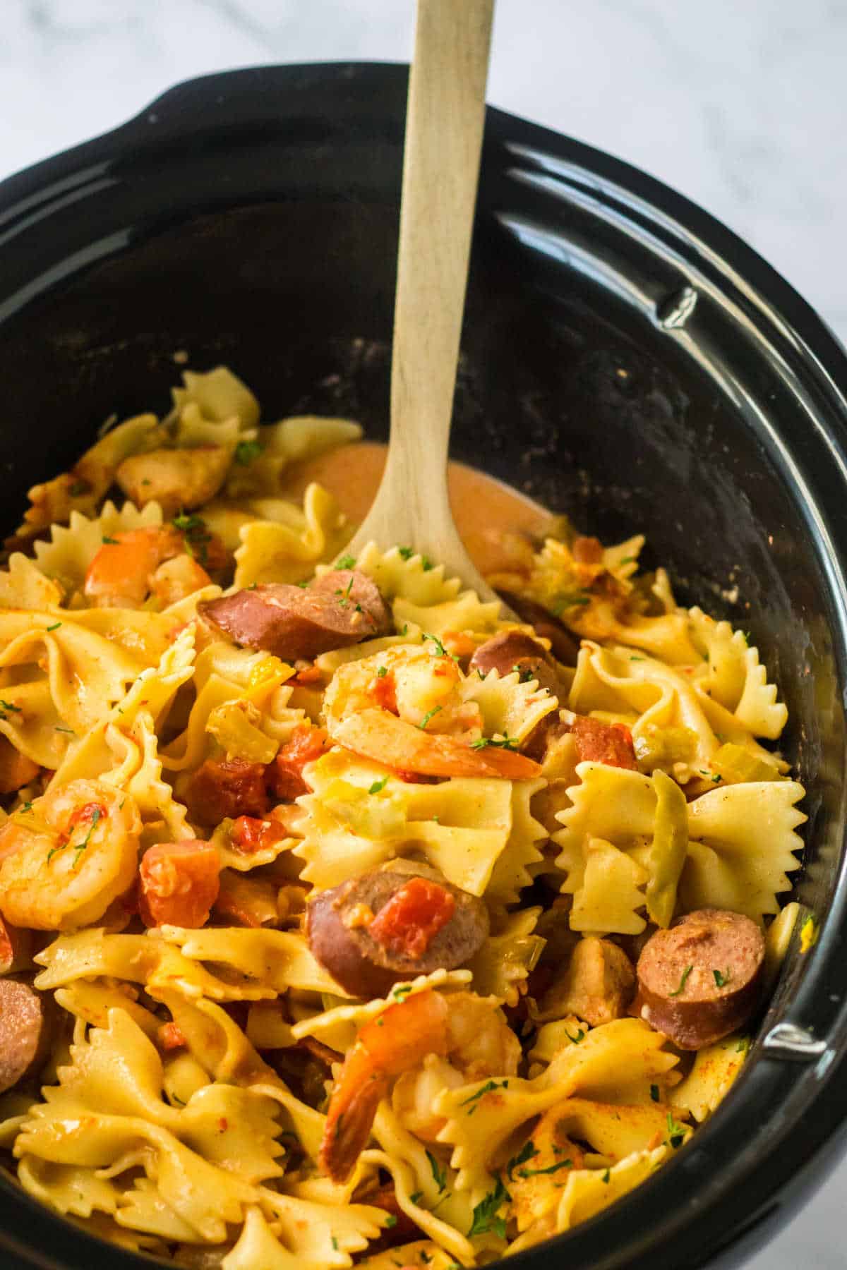 Jambalaya Pasta in a slow cooker with a wooden spoon.