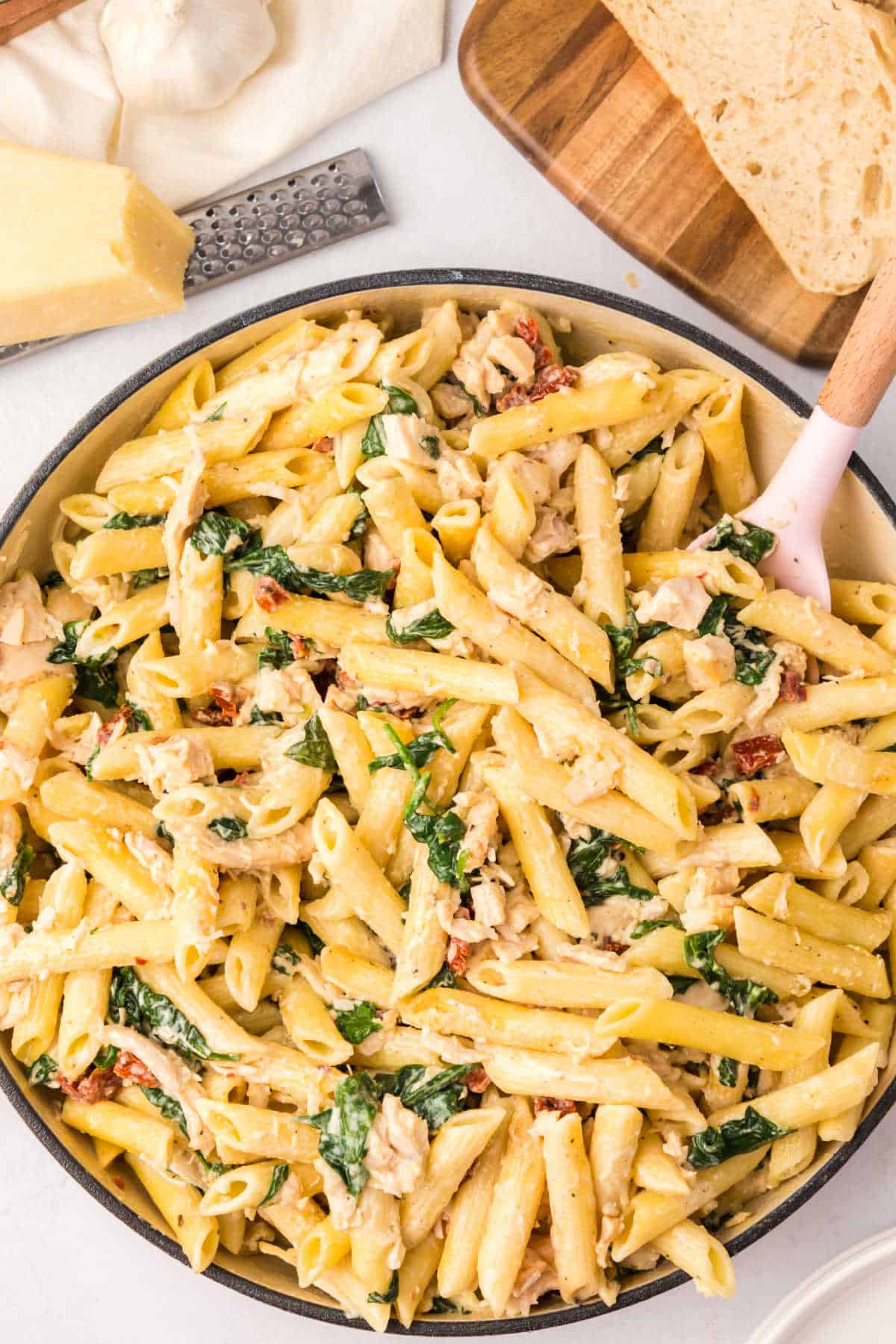 
Chicken and spinach pasta in a pan with a serving spoon.