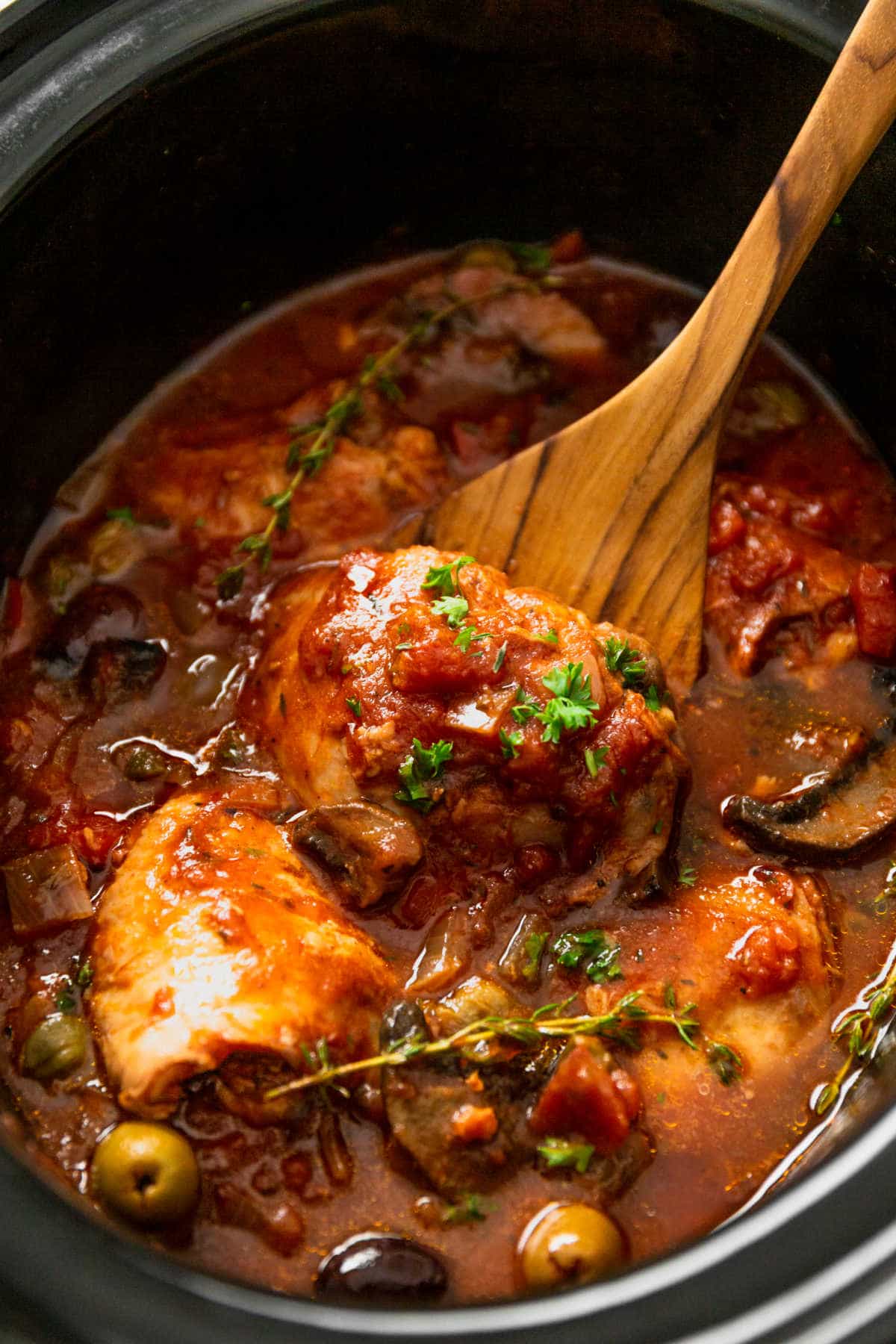 Chicken cacciatore in a slow cooker with a wooden spoon.