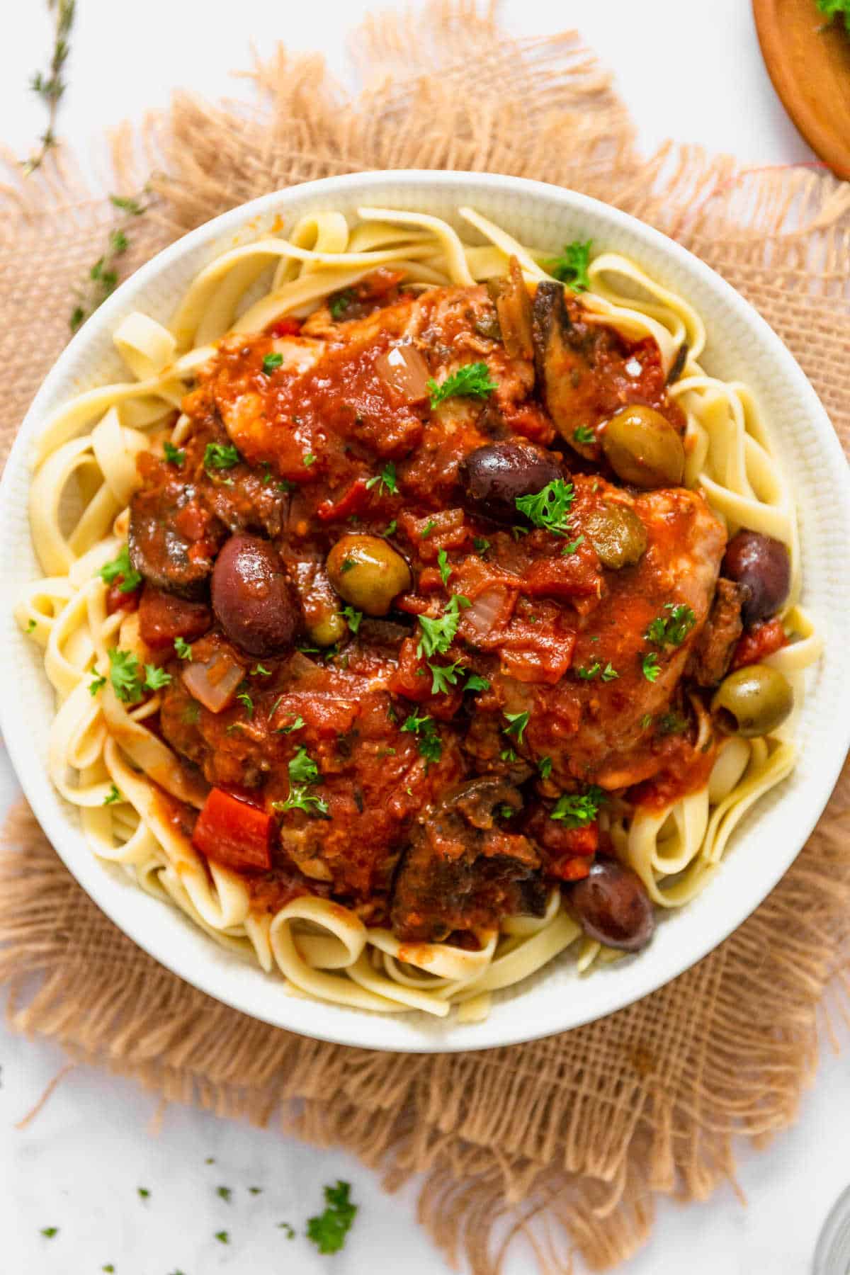 Chicken cacciatore on a bed of noodles on a plate.