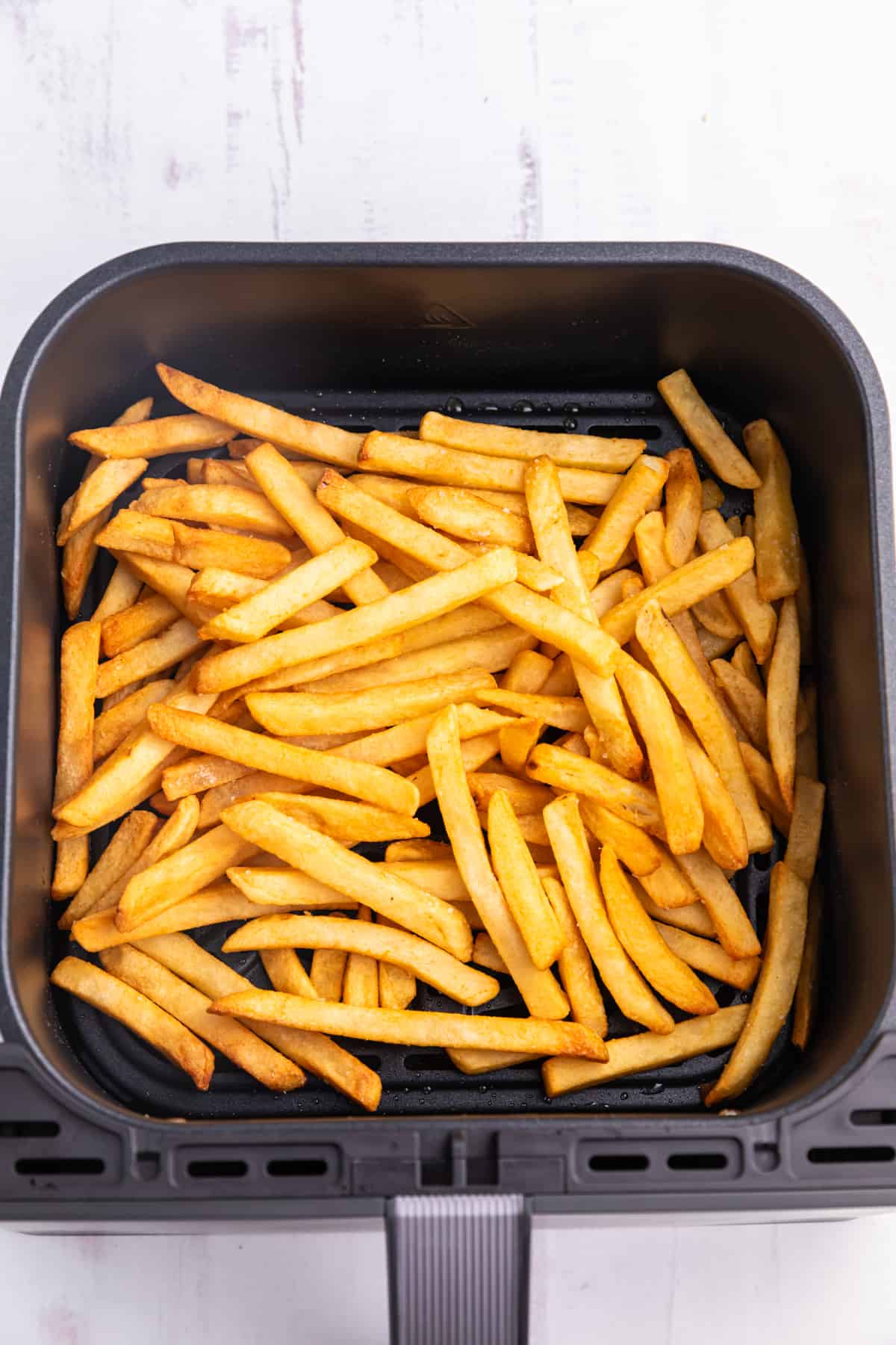 Frozen french fries in an air fryer basket.