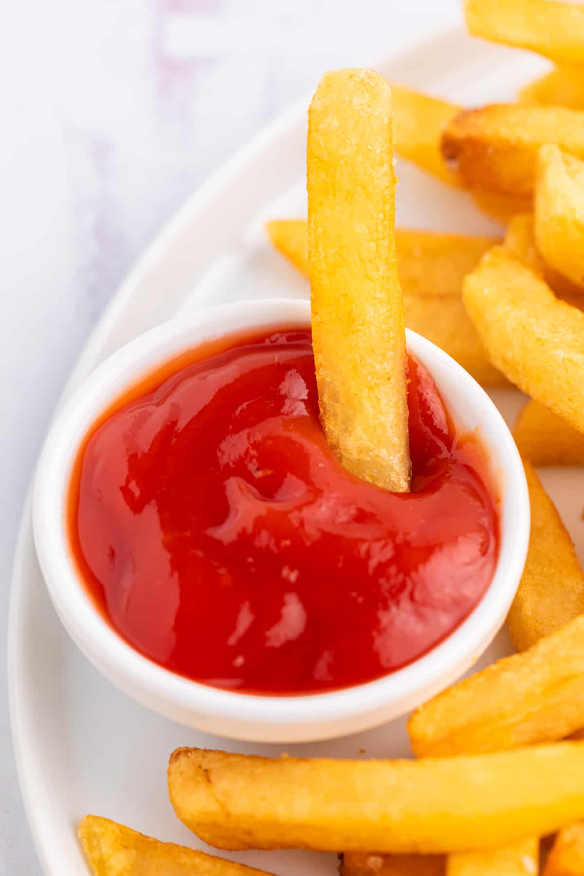 A french fry in a dipping sauce filled with ketchup.