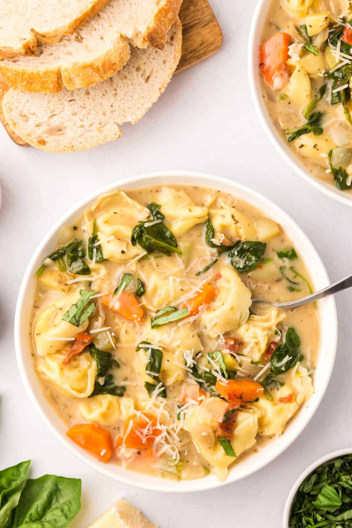 A bowl of creamy tortellini soup with a spoon.