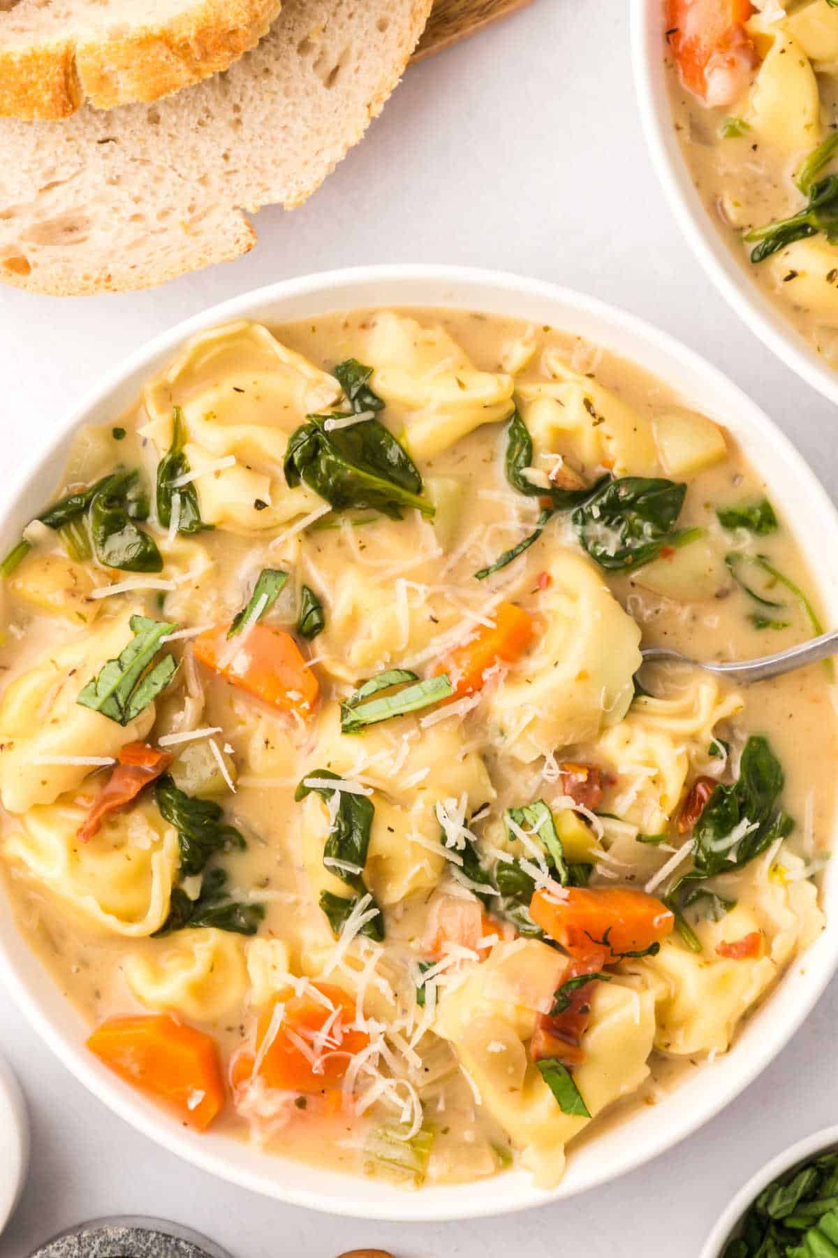 A bowl of creamy tortellini soup with a spoon in it.