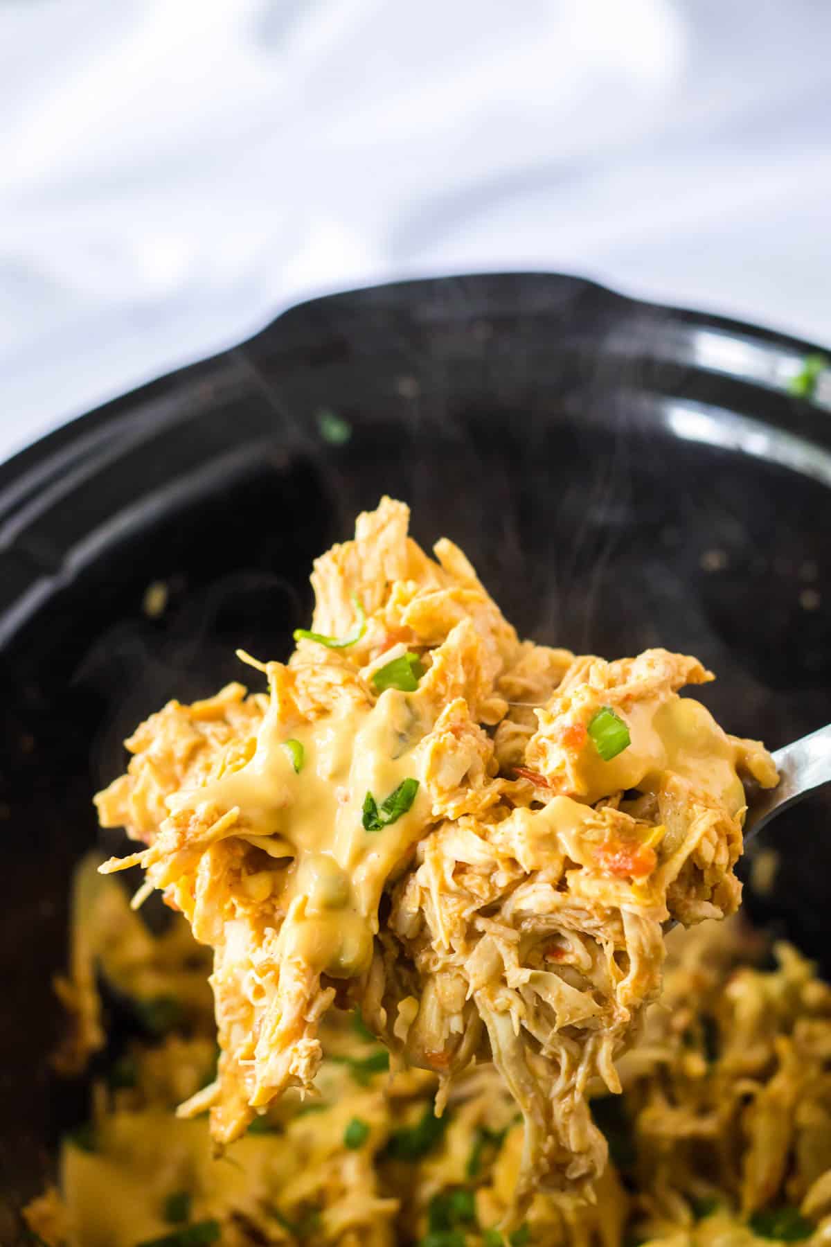 cheesy queso chicken being lifted out of a slow cooker