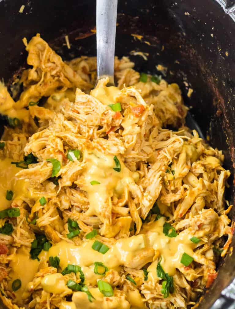 slow cooker queso chicken being spooned out