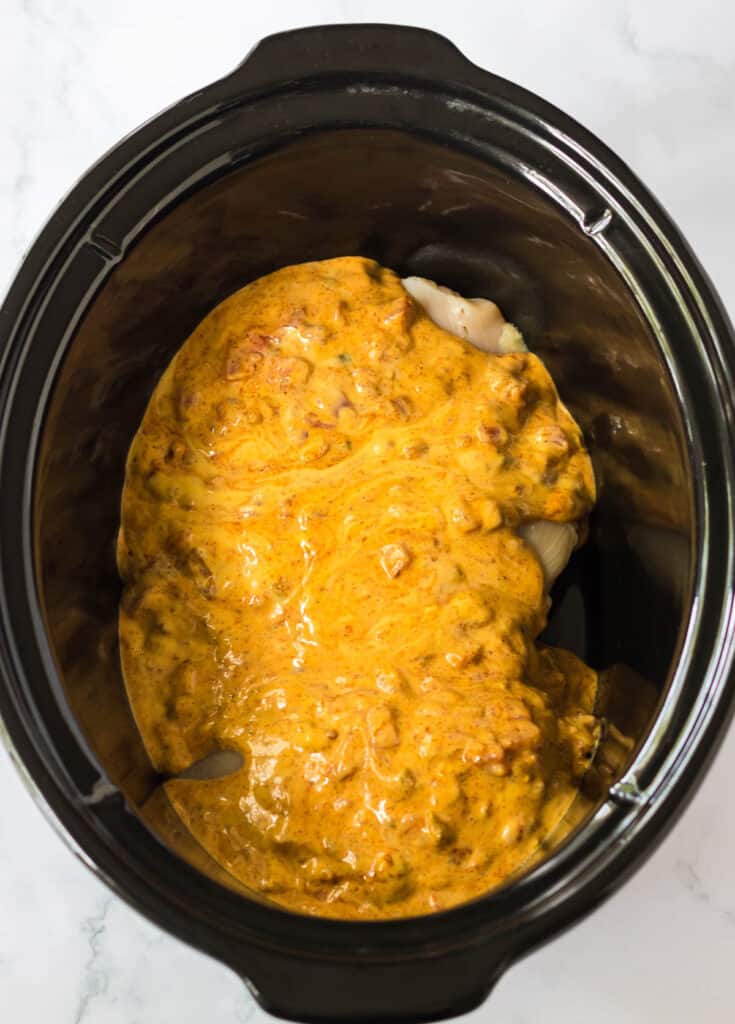 pouring queso and rotel over chicken in a crockpot