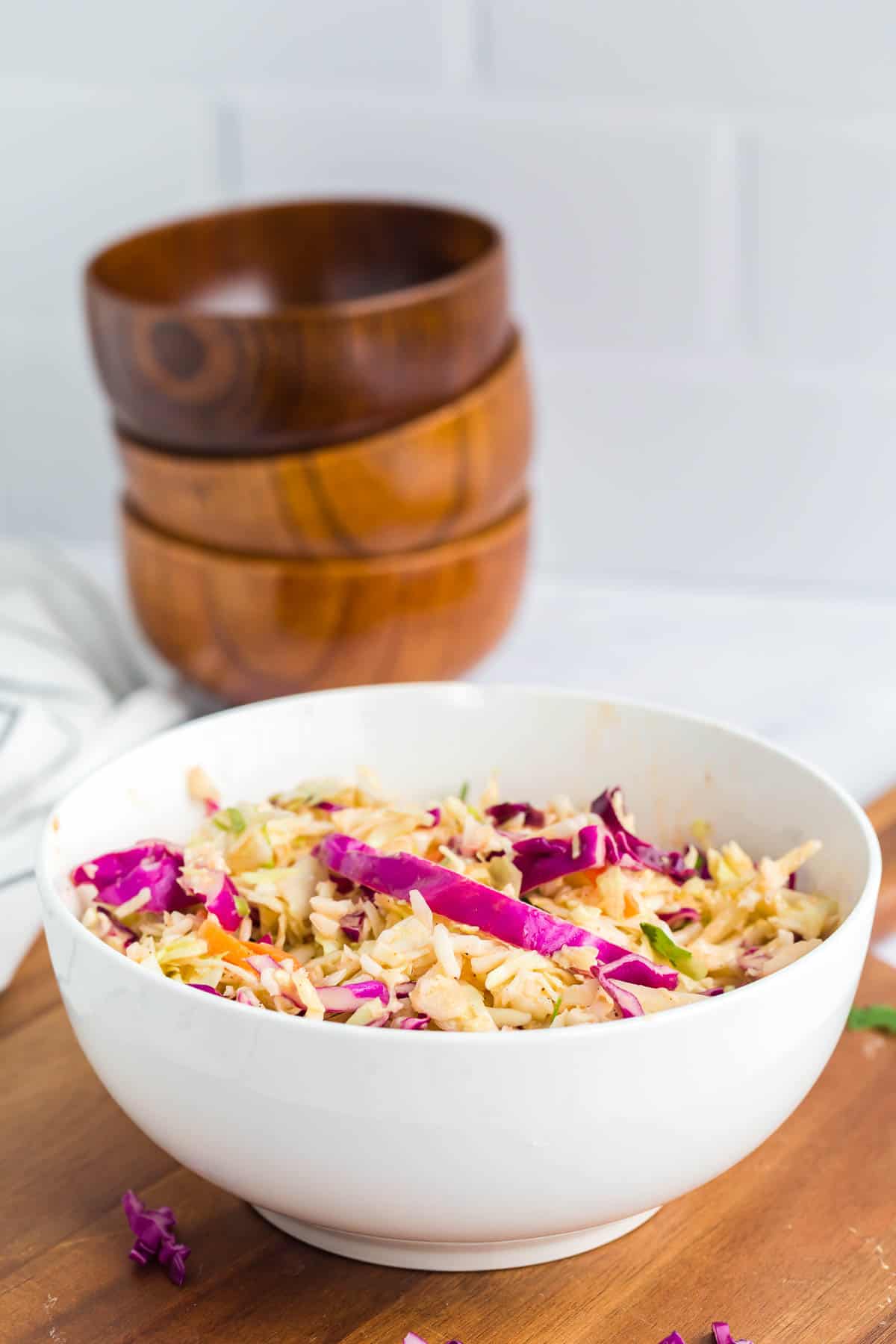 coleslaw salad in a white bowl with wooden bowls stacked in the background