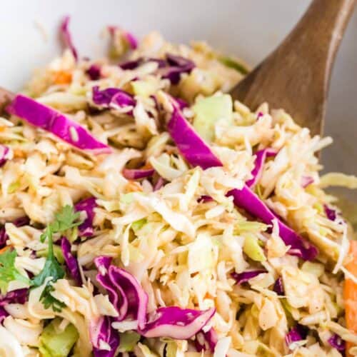 mixing spicy coleslaw together with wooden spoons