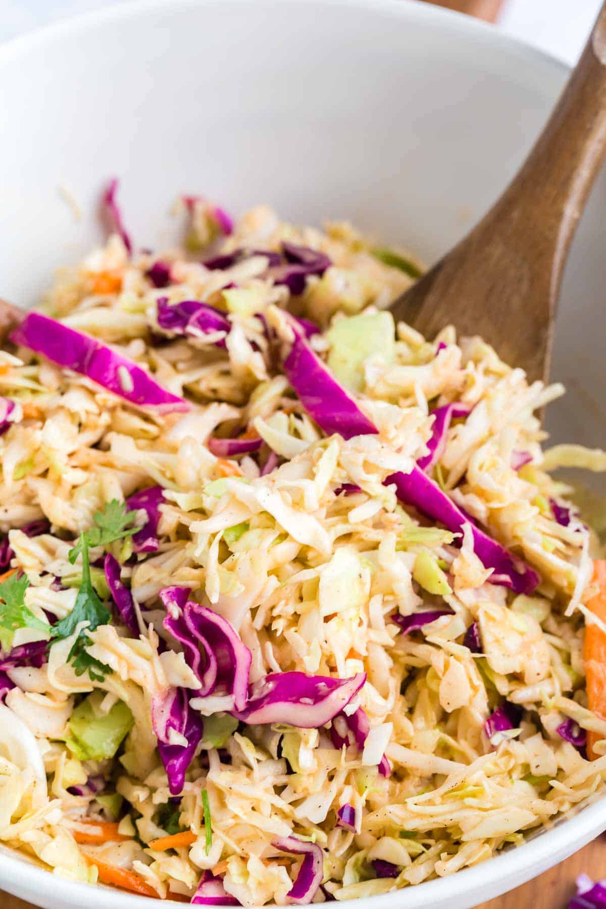 mixing spicy coleslaw together with wooden spoons