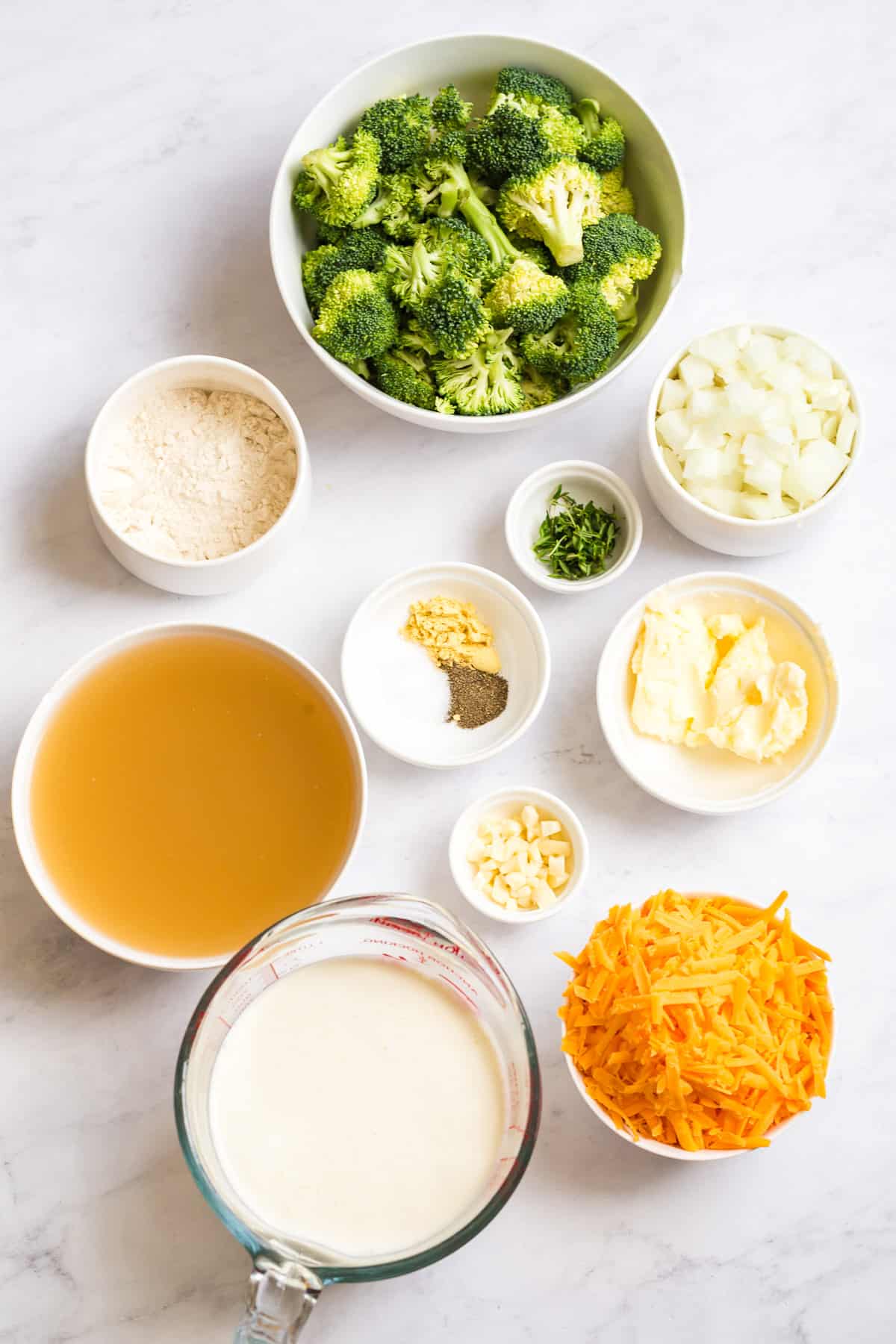 ingredients for broccoli cheddar soup in white bowls over a white marble background