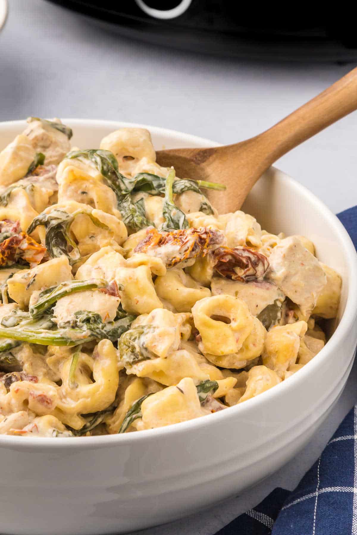 Tuscan chicken tortellini in a bowl with a wooden spoon.