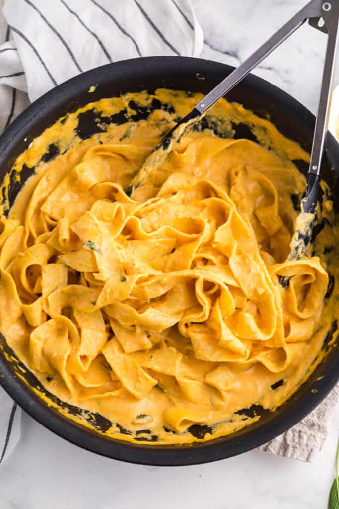 tossing pasta in pumpkin alfredo with tongs