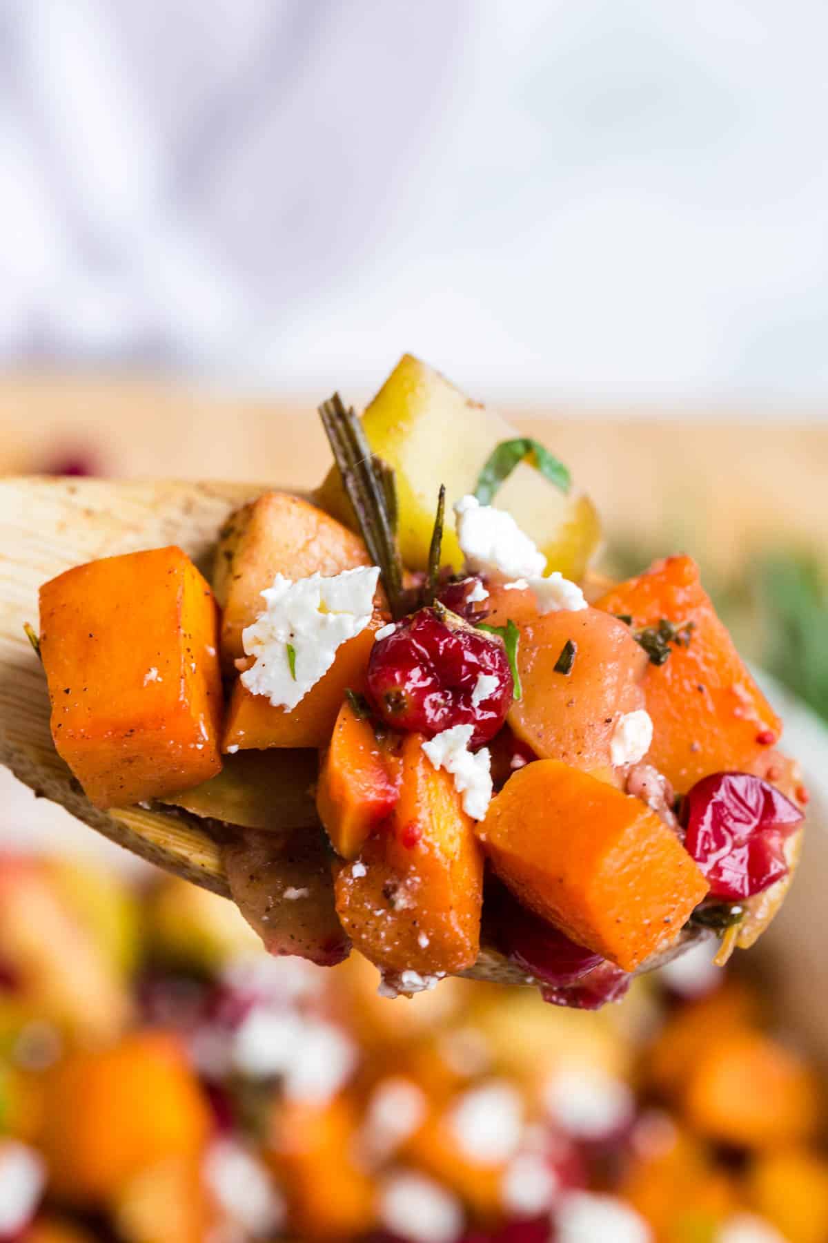 a wooden spoon with burst cranberries, feta cheese, and baked squash and apples