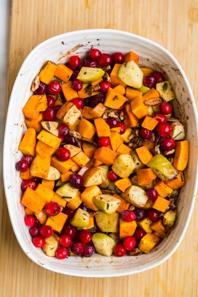 adding cranberries and pecans to baked butternut squash and apples