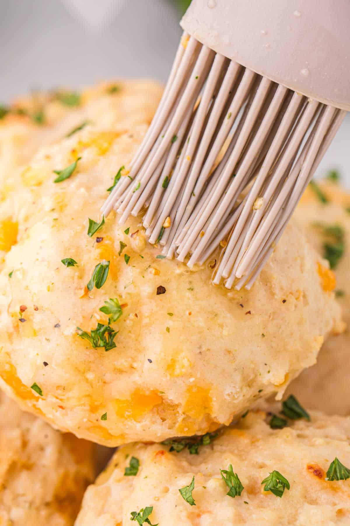 A pastry brush brushing garlic butter on copycat Red Lobster biscuits.