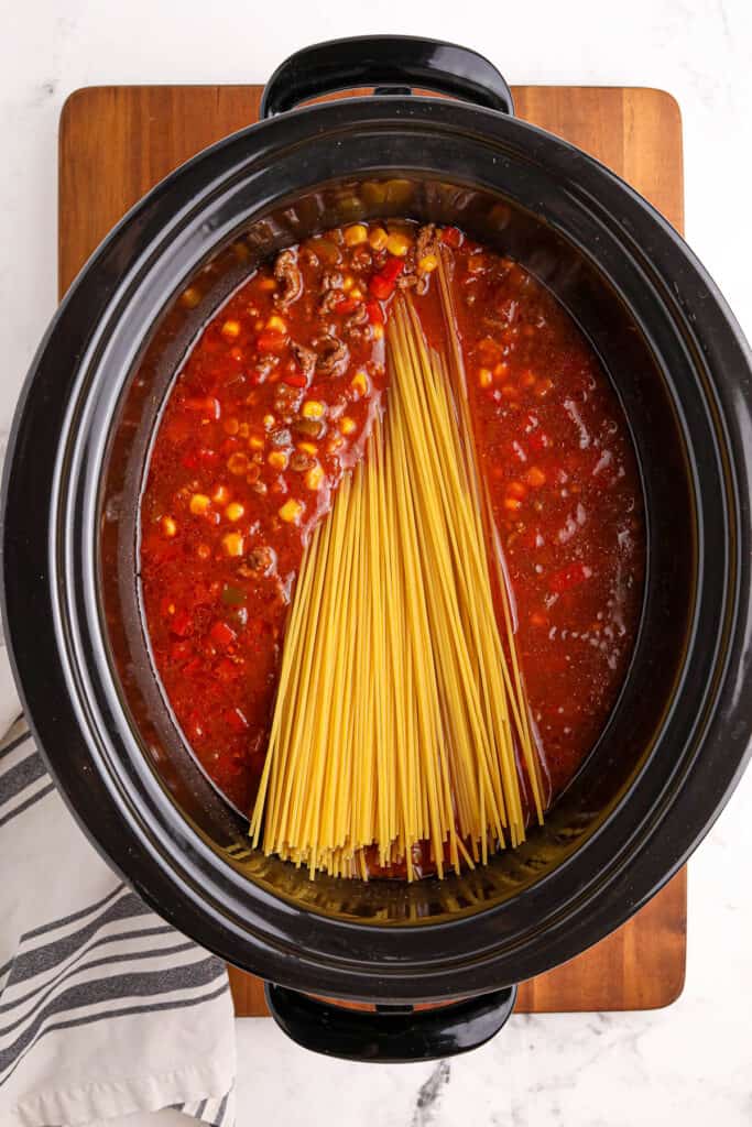 adding spaghetti noodles to the slow cooker for a taco spaghetti recipe