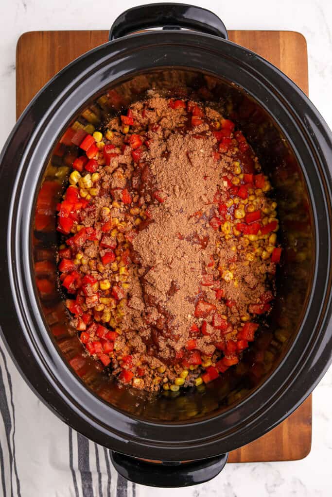 adding taco seasoning to a slow cooker with ground beef and vegetables