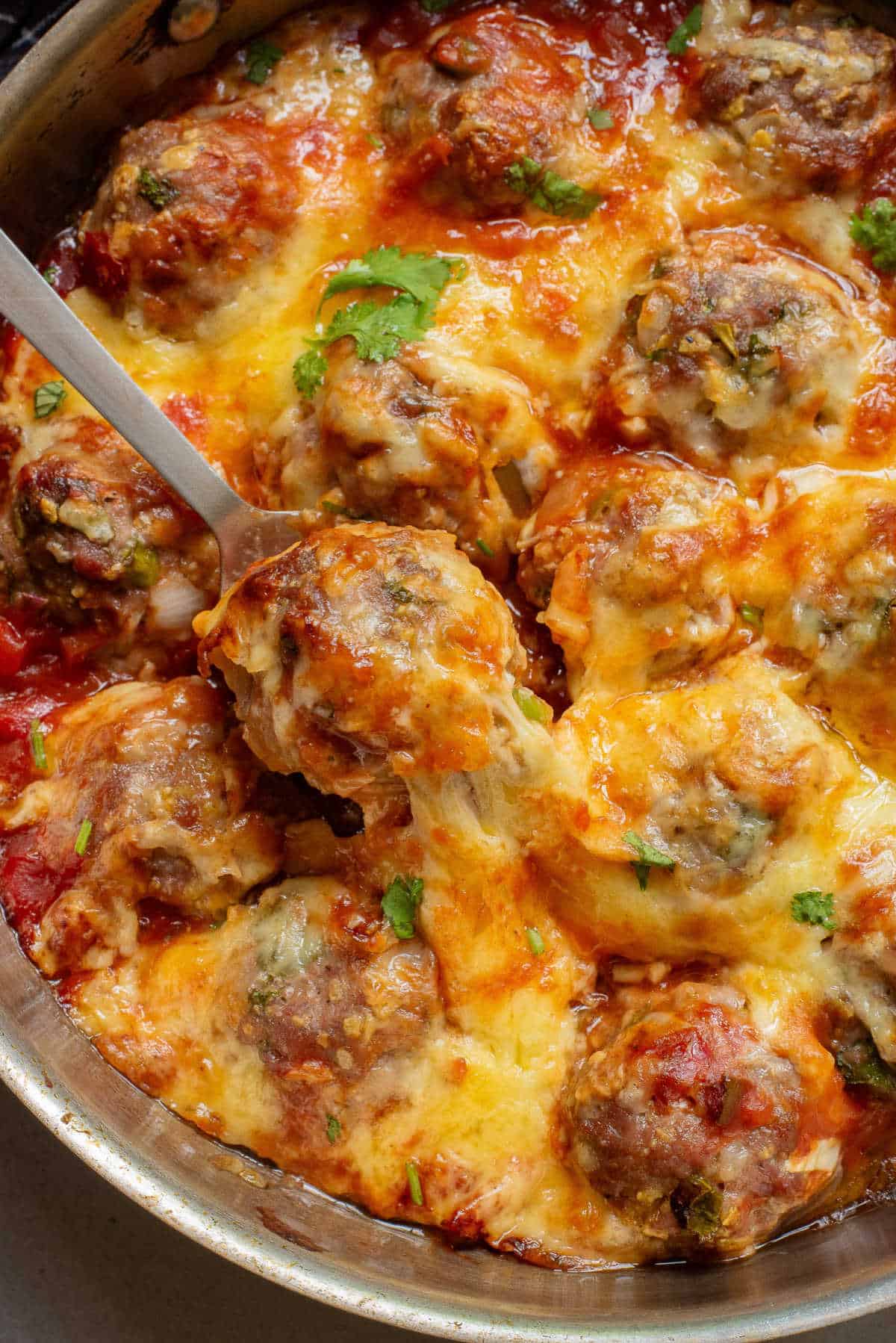Baked Mexican Meatballs in a skillet with a serving spoon.