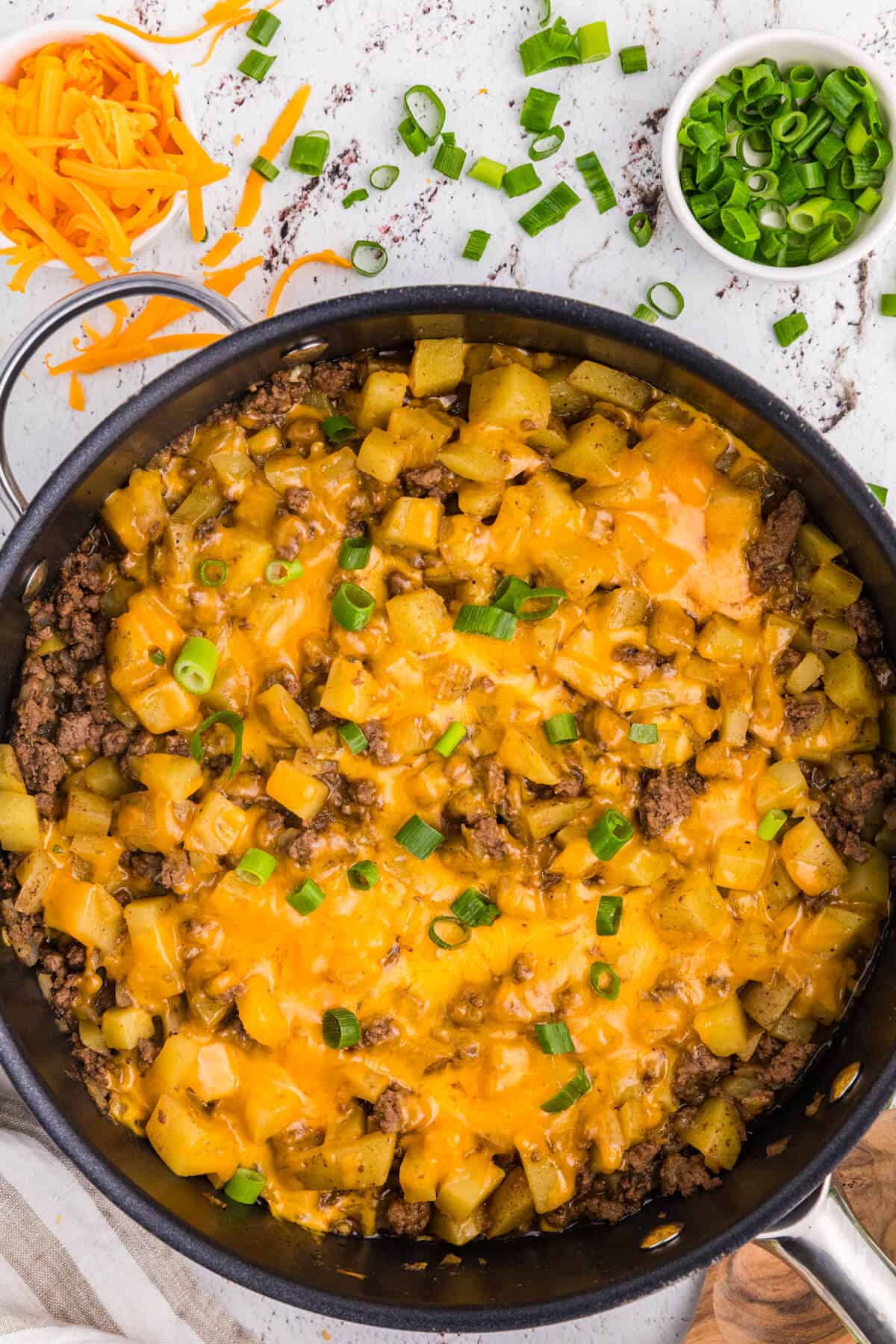 Cheesy Ground Beef and Potato Skillet with tender diced potatoes, melted cheddar cheese, and sliced green onions in a large black skillet.