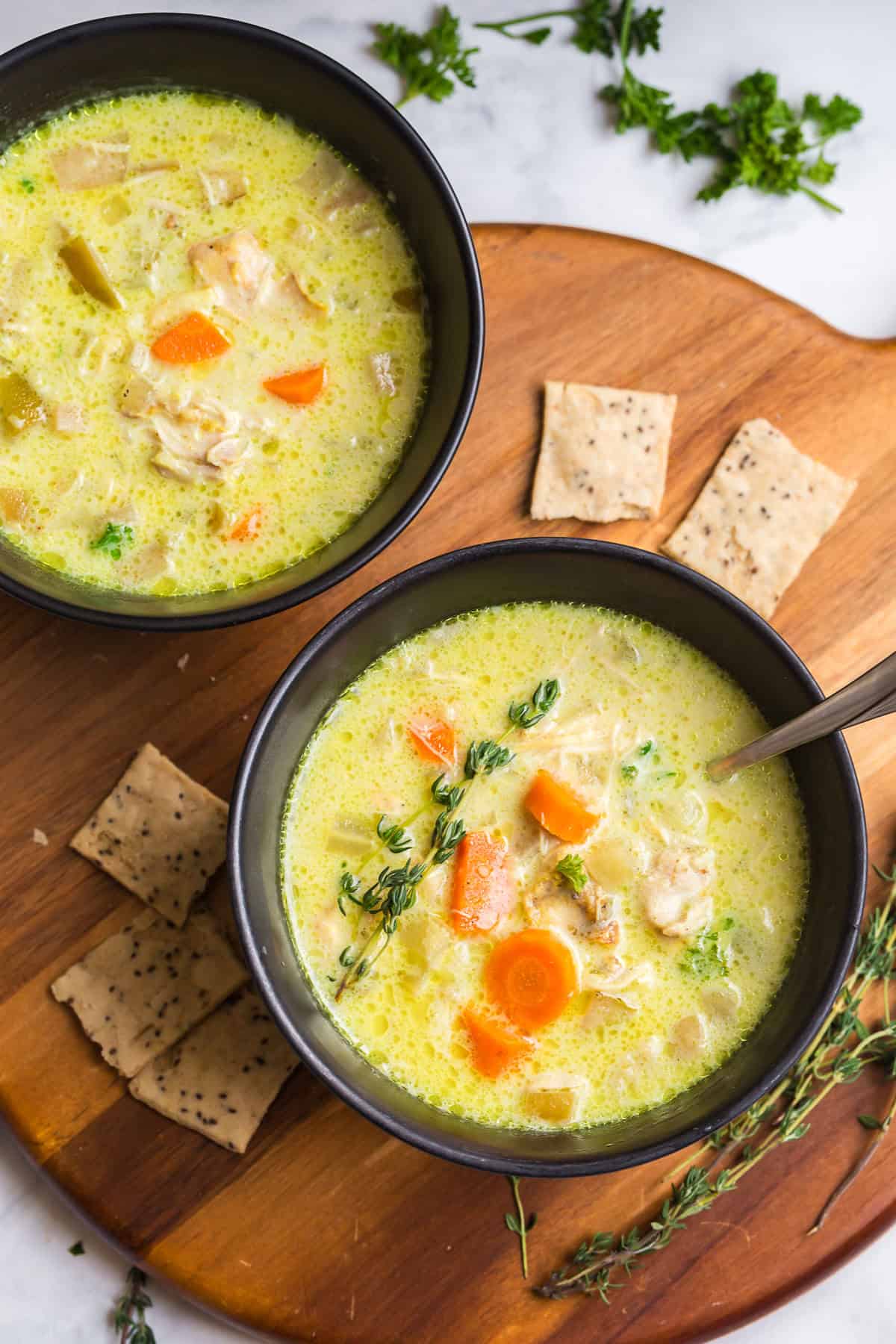 Two bowls of slow cooker mulligatawny soup on a wooden board with crackers and fresh thyme.