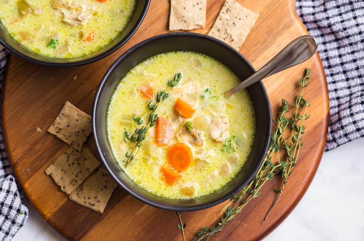 Bowl of mulligatawny soup with a spoon, crackers, and fresh thyme on a wooden serving board.