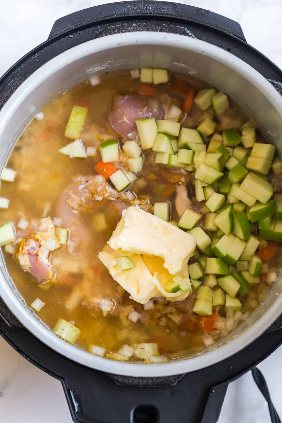 Butter, chicken thighs, apples, and aromatics in a slow cooker